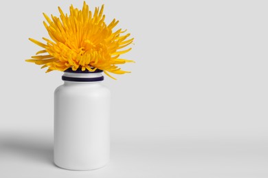 Photo of Plastic medicine bottle and yellow flower on white background, space for text. Medicament