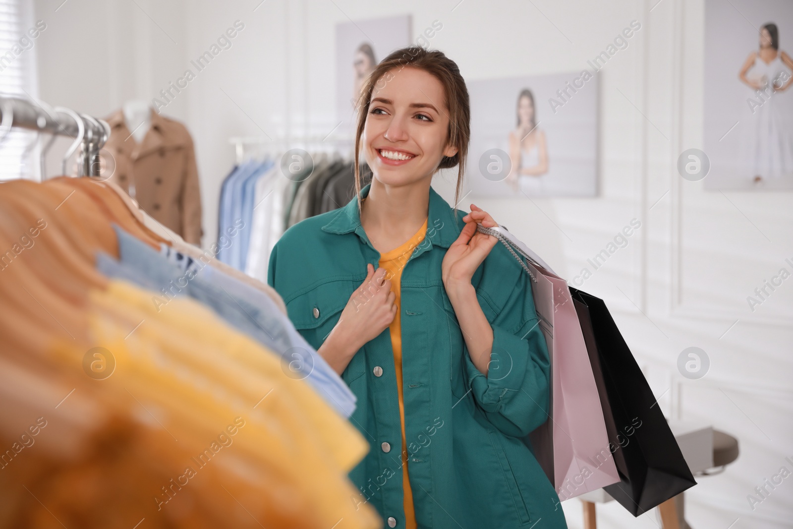 Photo of Young woman holding shopping bags near rack with clothes in modern boutique