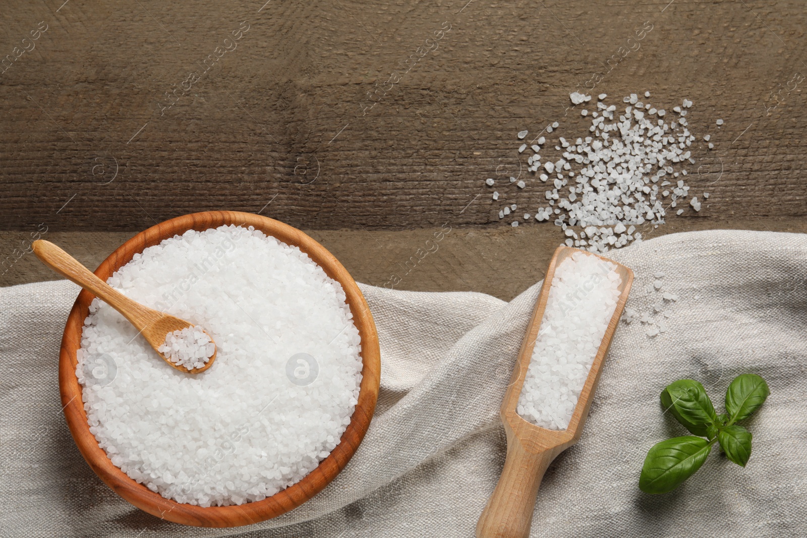 Photo of Natural sea salt and basil leaf on wooden table, flat lay. Space for text