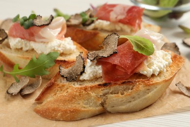 Photo of Delicious bruschettas with cheese, prosciutto and slices of black truffle on white wooden table, closeup