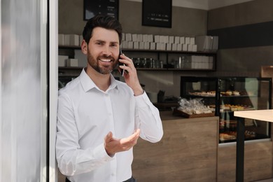 Photo of Happy business owner talking on phone in bakery shop. Space for text