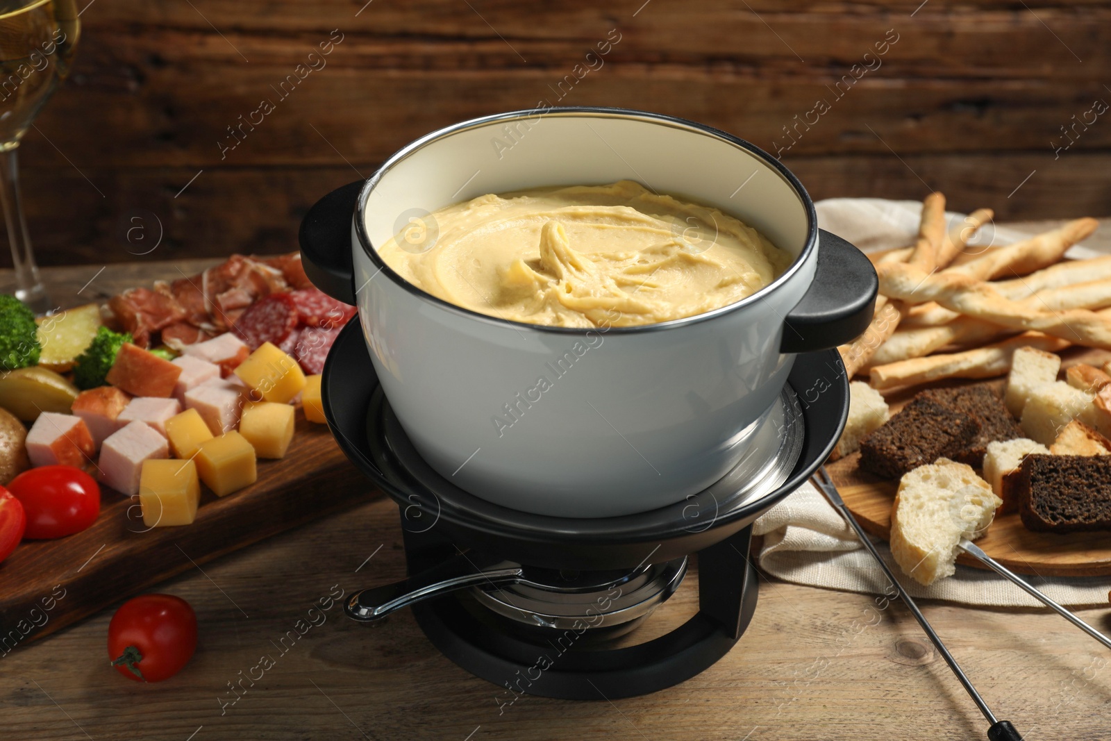 Photo of Tasty melted cheese in fondue pot and snacks on wooden table, closeup