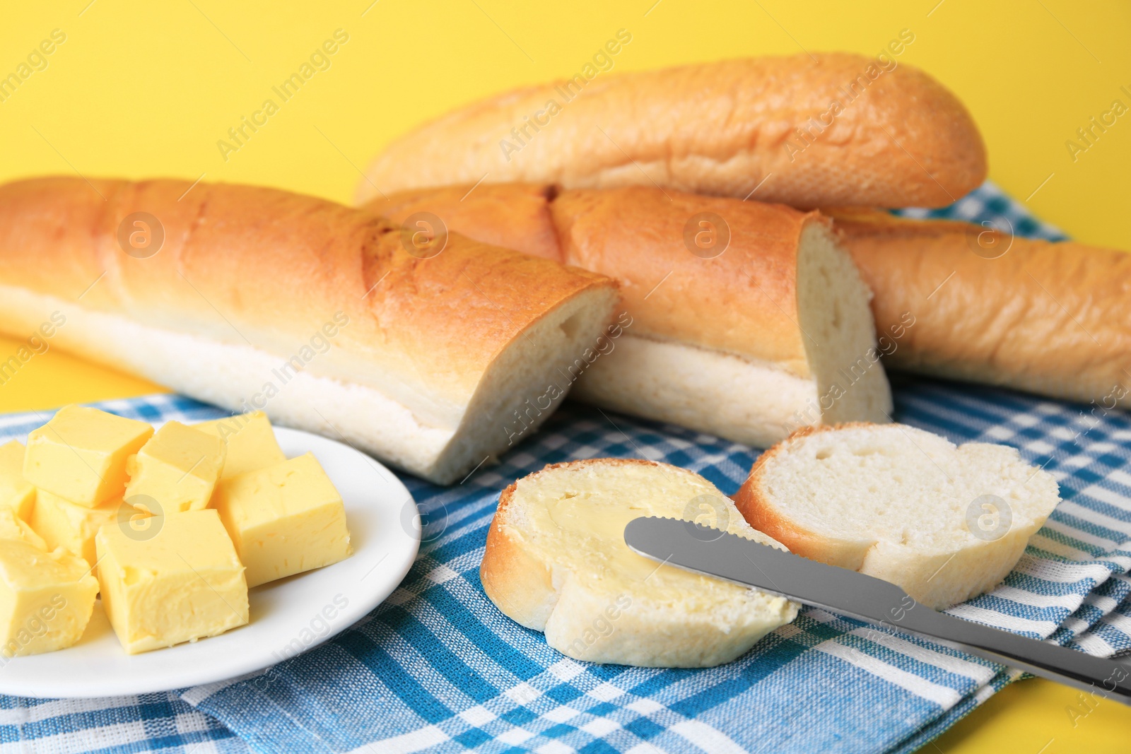 Photo of Whole and cut baguettes with fresh butter on yellow background, closeup