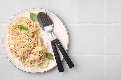 Photo of Plate of tasty pasta Carbonara with basil leaves on white tiled table, top view. Space for text