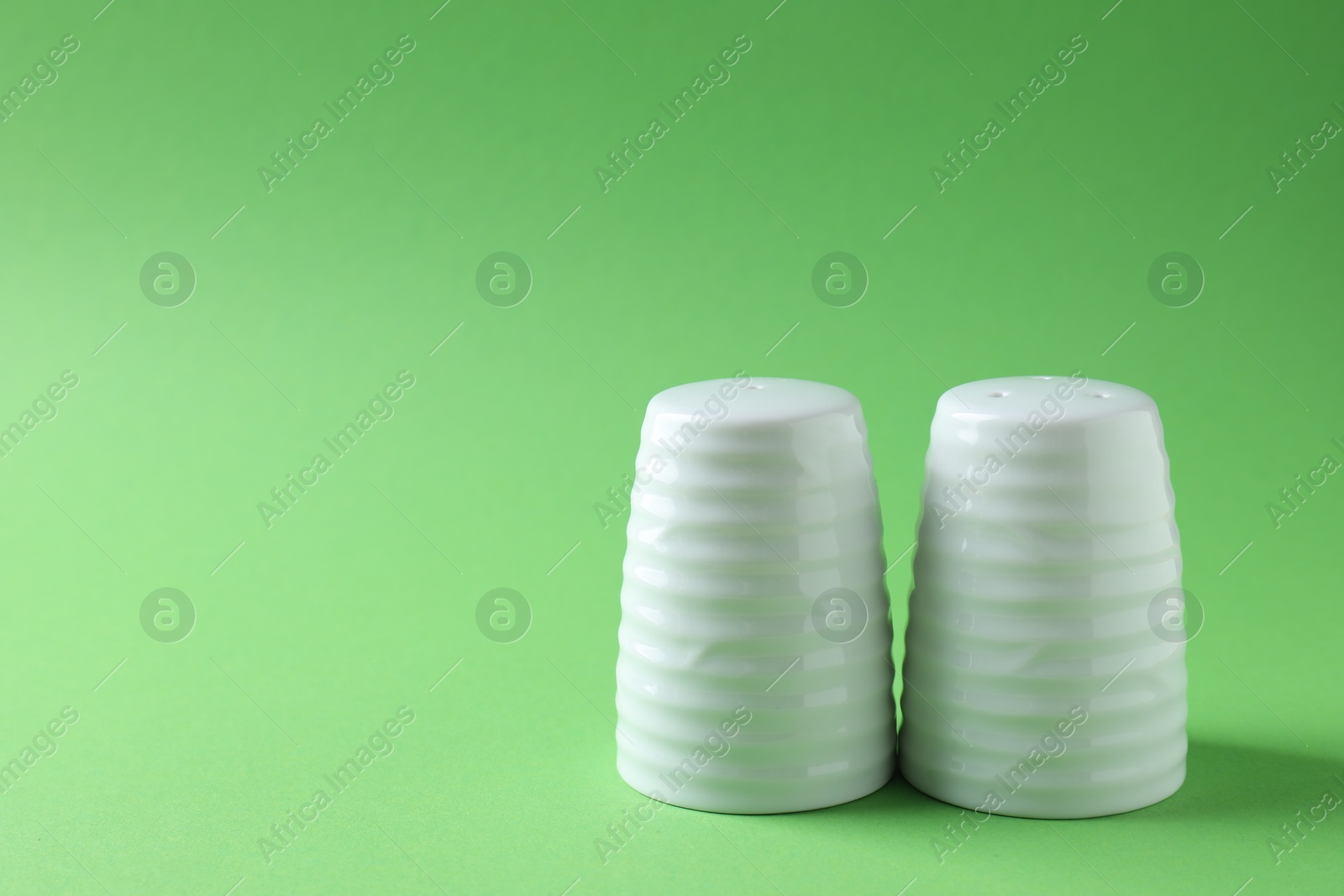 Photo of Salt and pepper shakers on green background, closeup. Space for text