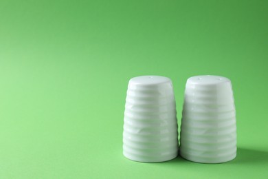 Photo of Salt and pepper shakers on green background, closeup. Space for text