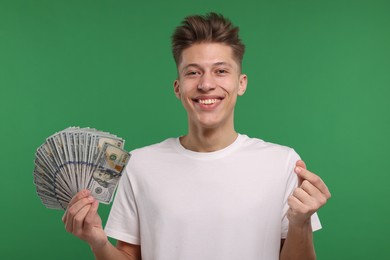 Happy man with dollar banknotes showing money gesture on green background