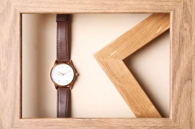 Stylish wristwatch with leather band in wooden frame on beige background