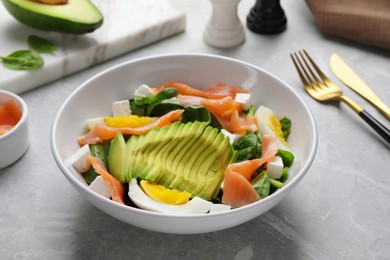 Delicious salad with boiled egg, salmon and avocado on light grey marble table, closeup