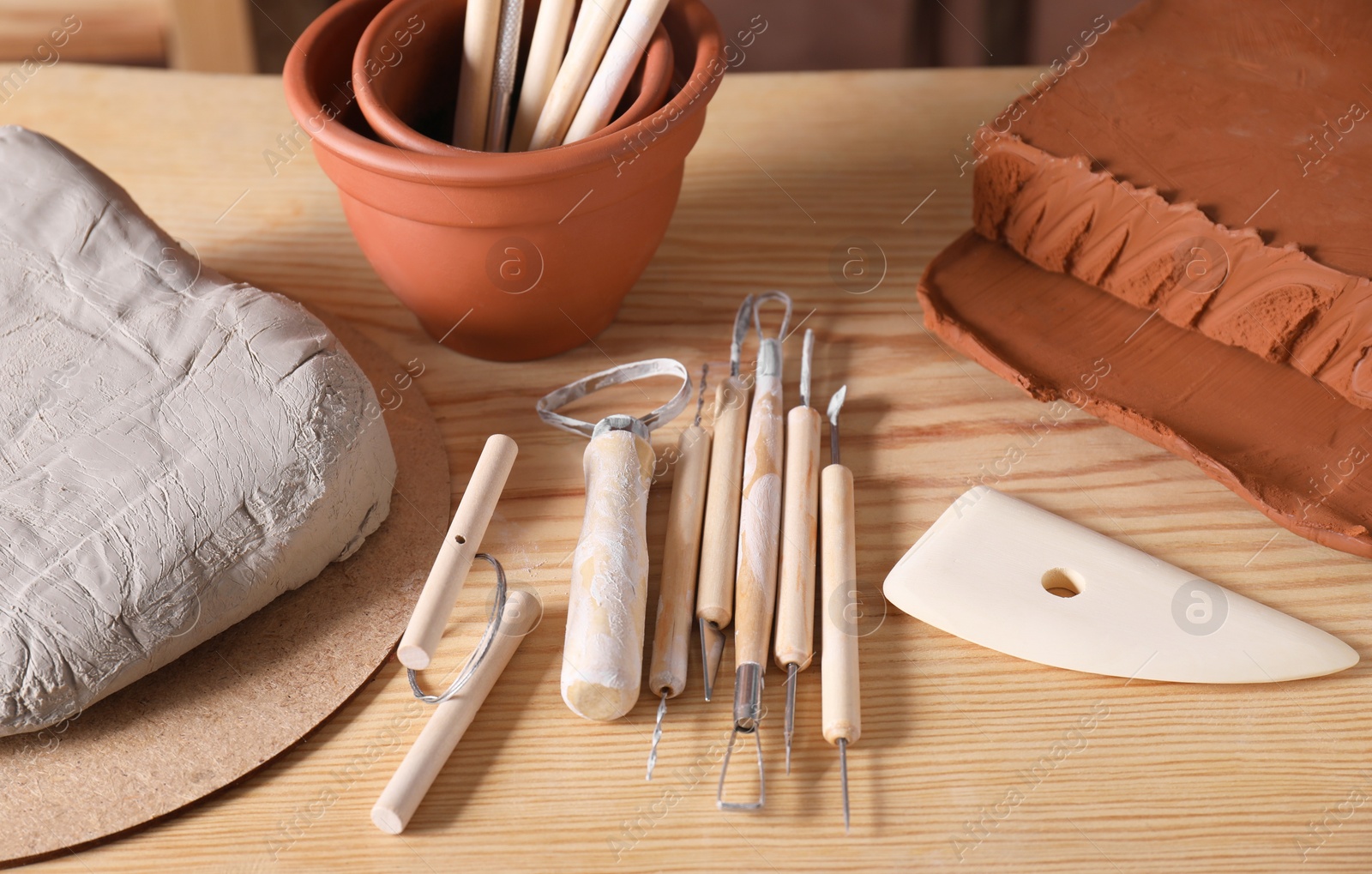 Photo of Clay and set of modeling tools on wooden table in workshop