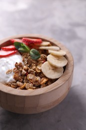 Photo of Tasty granola with yogurt, banana and strawberry in bowl on gray textured table, closeup