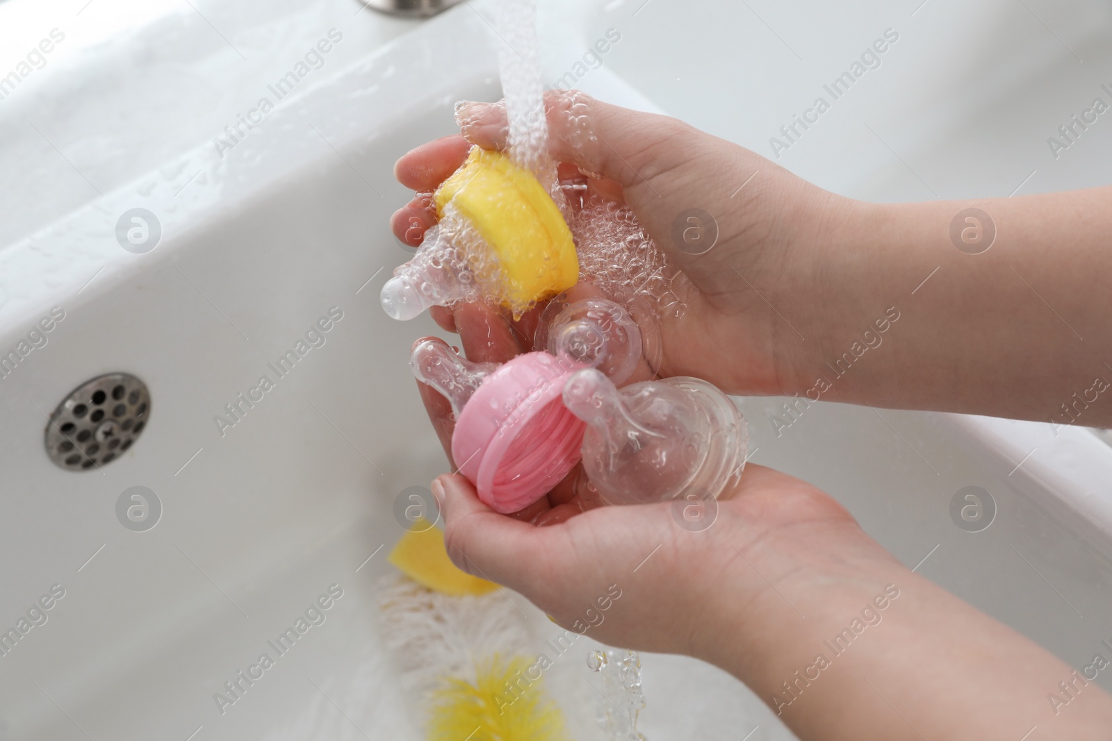 Photo of Woman washing baby bottle nipples under stream of water, above view