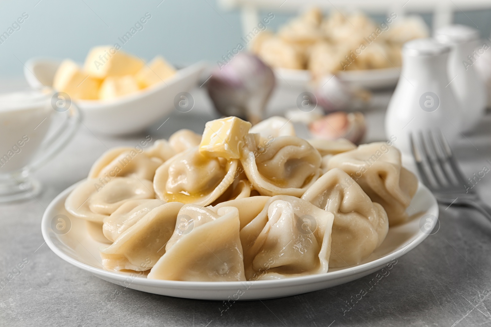 Photo of Tasty dumplings with butter on light grey table against blurred background