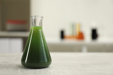 Photo of Flask with green crude oil on light grey table, space for text