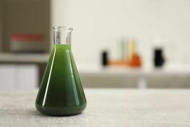 Flask with green crude oil on light grey table, space for text