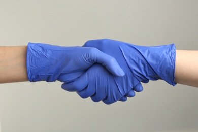 Photo of People in medical gloves shaking hands on grey background, closeup