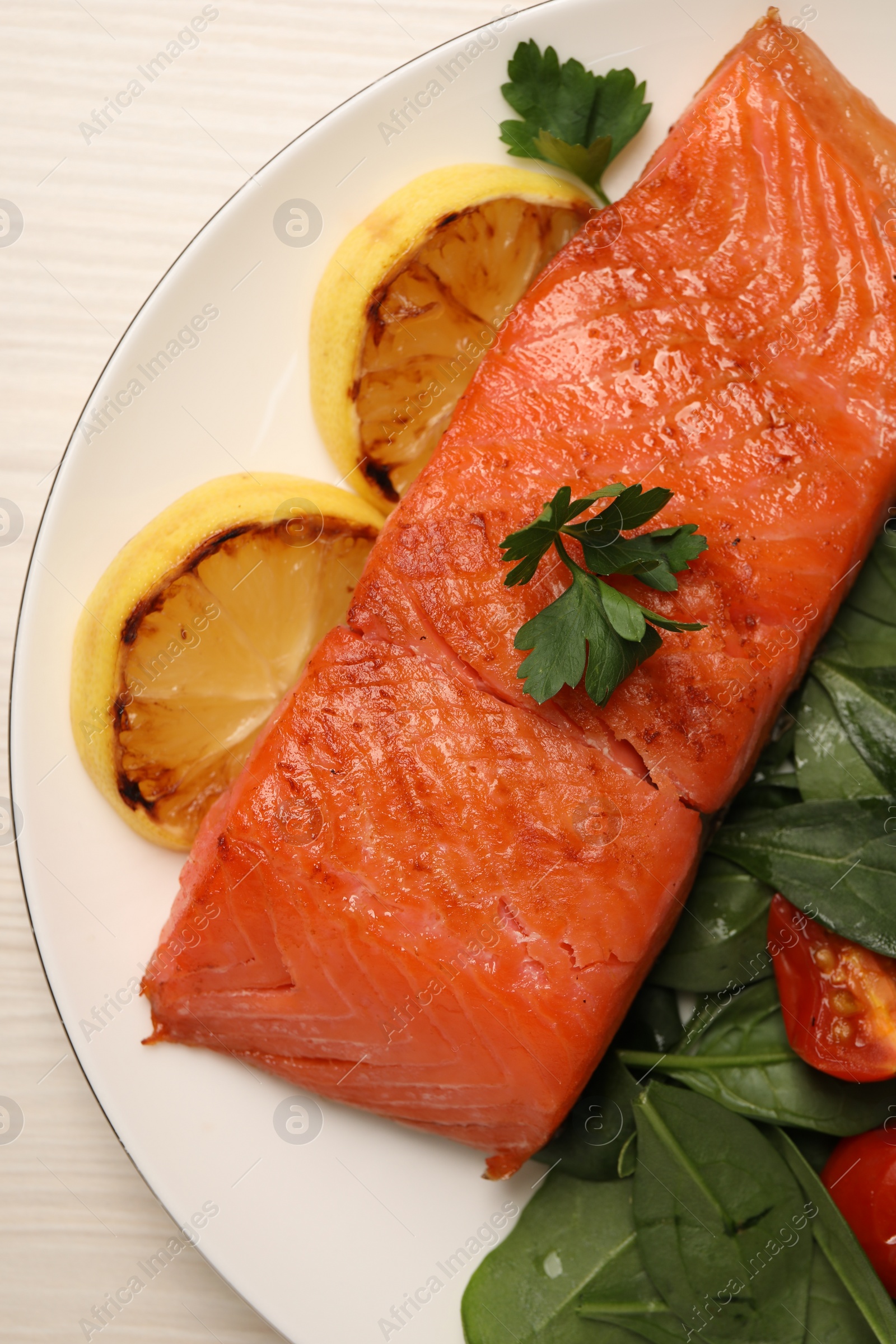 Photo of Tasty grilled salmon with basil, tomatoes and lemon on white wooden table, top view