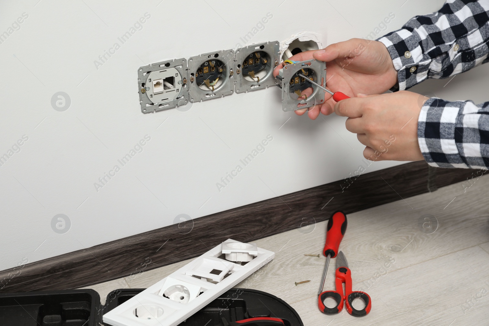 Photo of Electrician with screwdriver repairing power sockets indoors, closeup