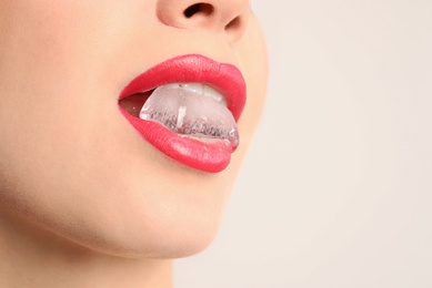 Photo of Young woman holding ice cube in mouth on light background, closeup. Space for text