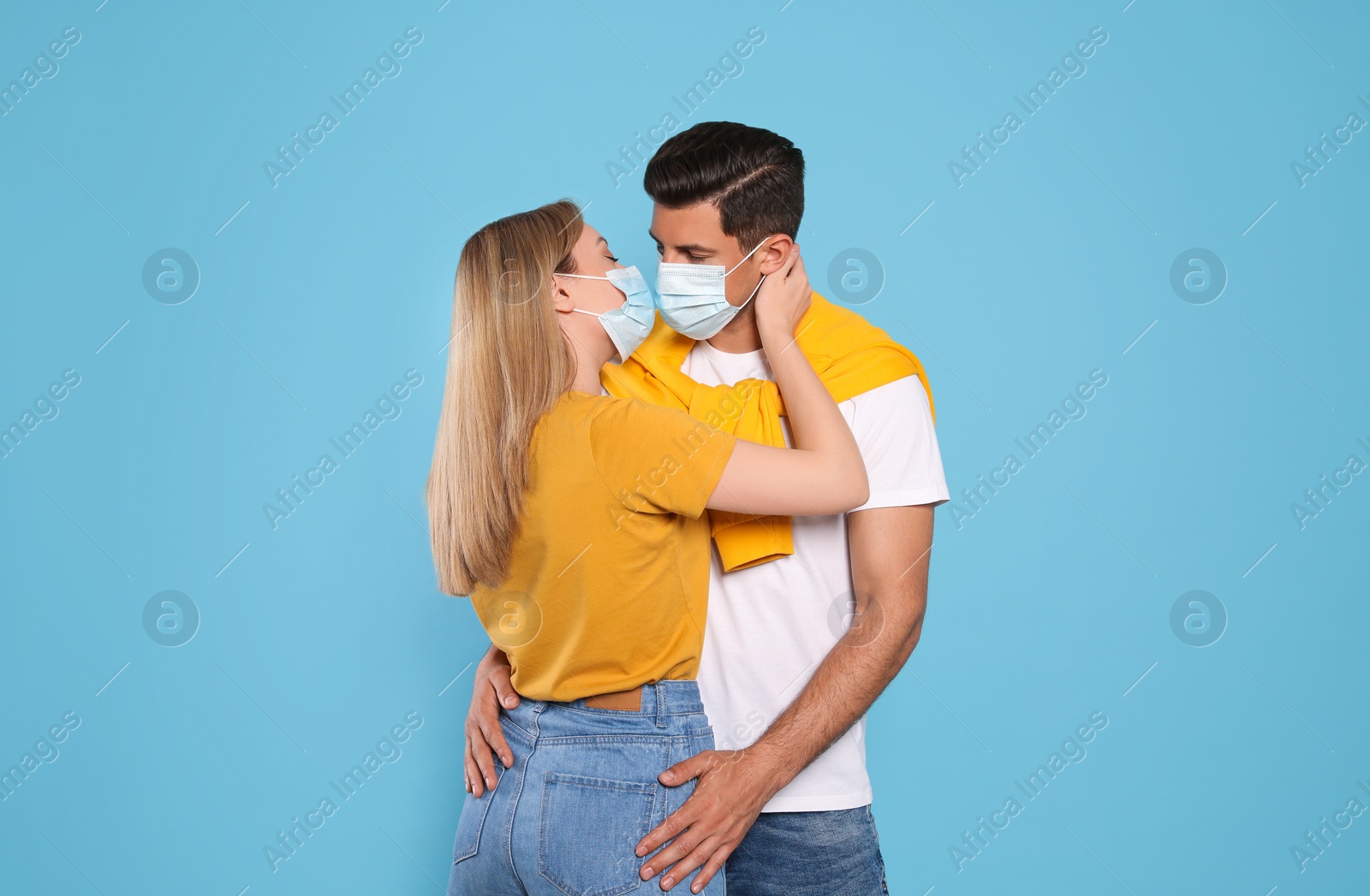 Photo of Couple in medical masks trying to kiss on light blue background