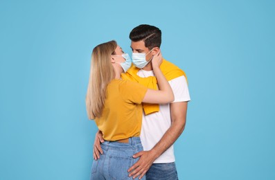 Photo of Couple in medical masks trying to kiss on light blue background