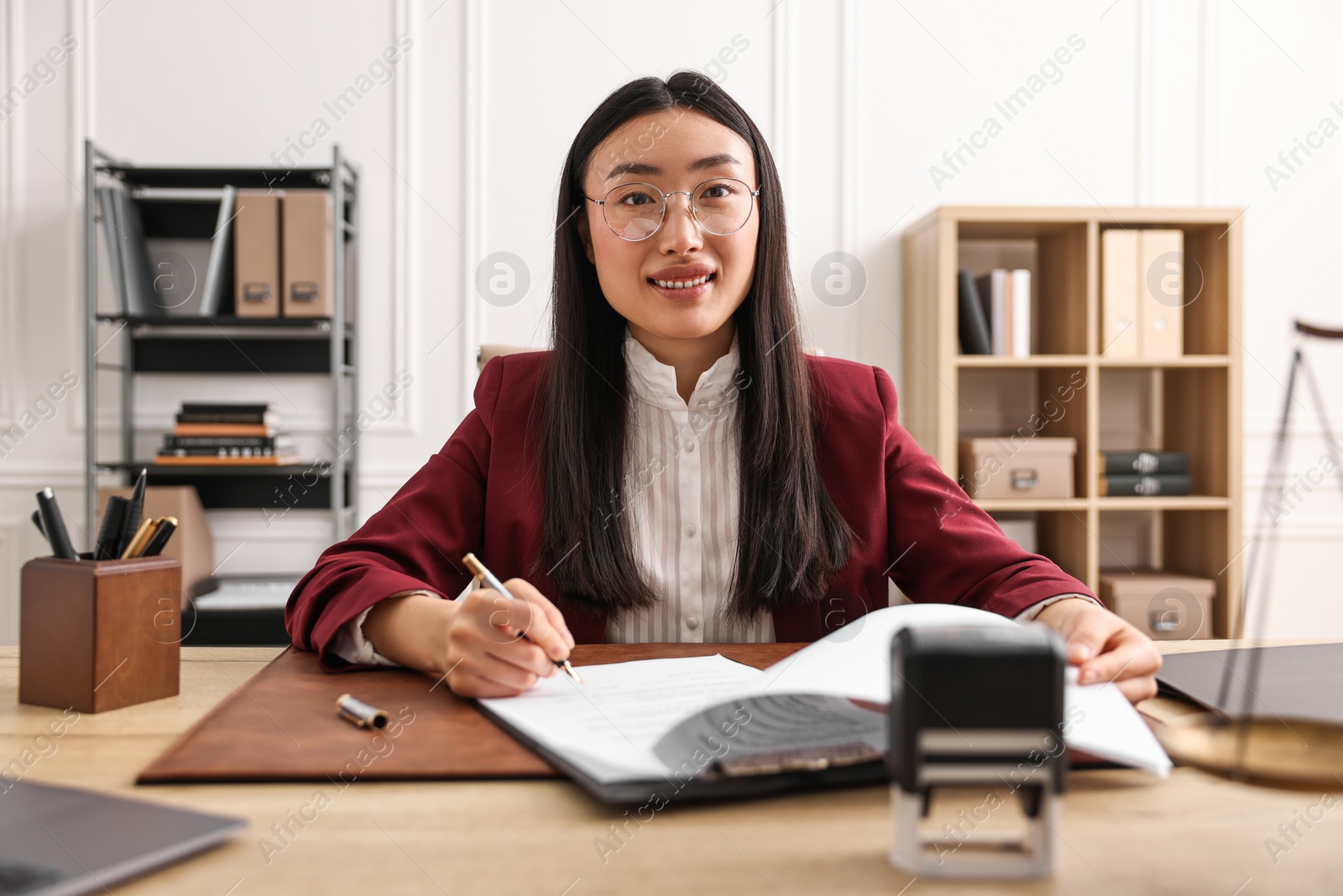 Photo of Smiling notary signing document at table in office