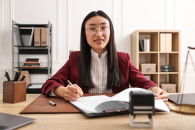 Smiling notary signing document at table in office