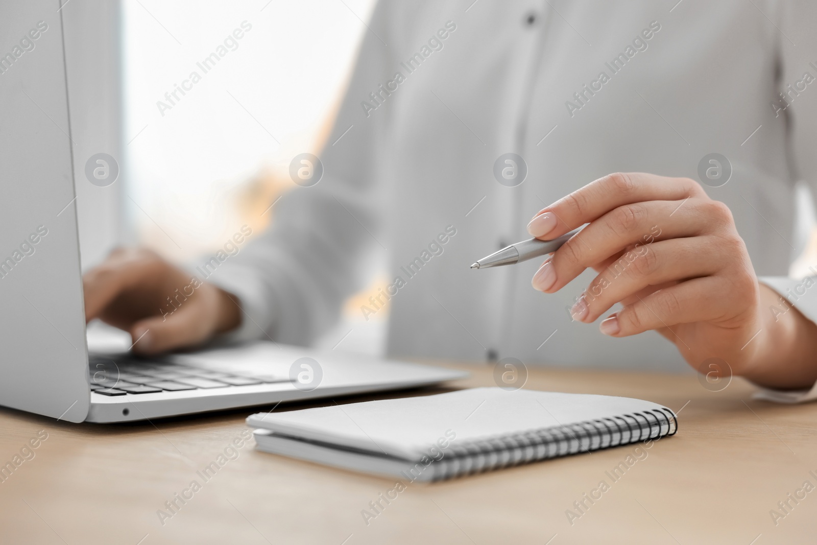 Photo of Woman with notebook and pen working on laptop at wooden table, closeup. Electronic document management