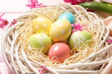 Wicker nest with colorful painted Easter eggs on table, closeup