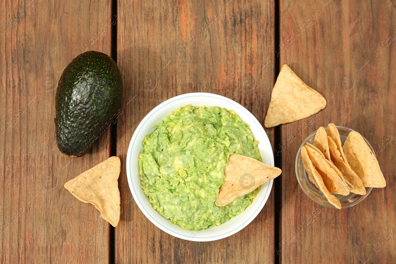 Photo of Delicious guacamole, avocado and nachos on wooden table, flat lay