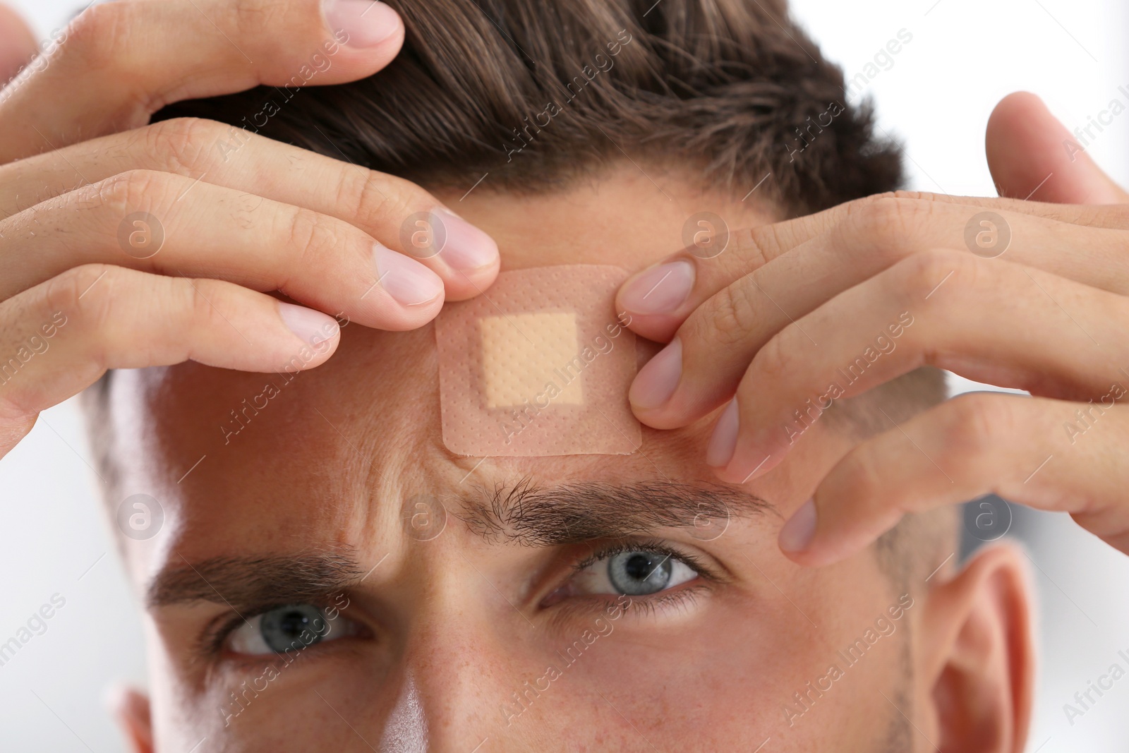 Photo of Man applying adhesive bandage on forehead indoors, closeup