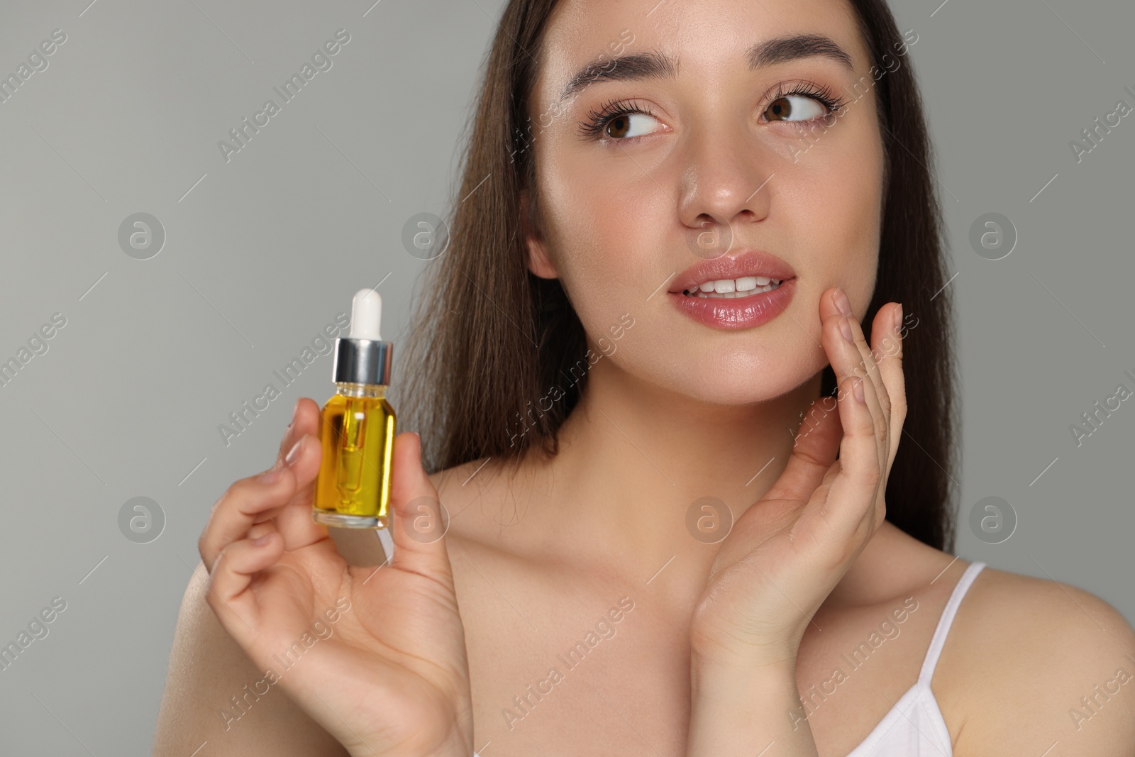 Photo of Beautiful young woman with essential oil on light grey background, closeup