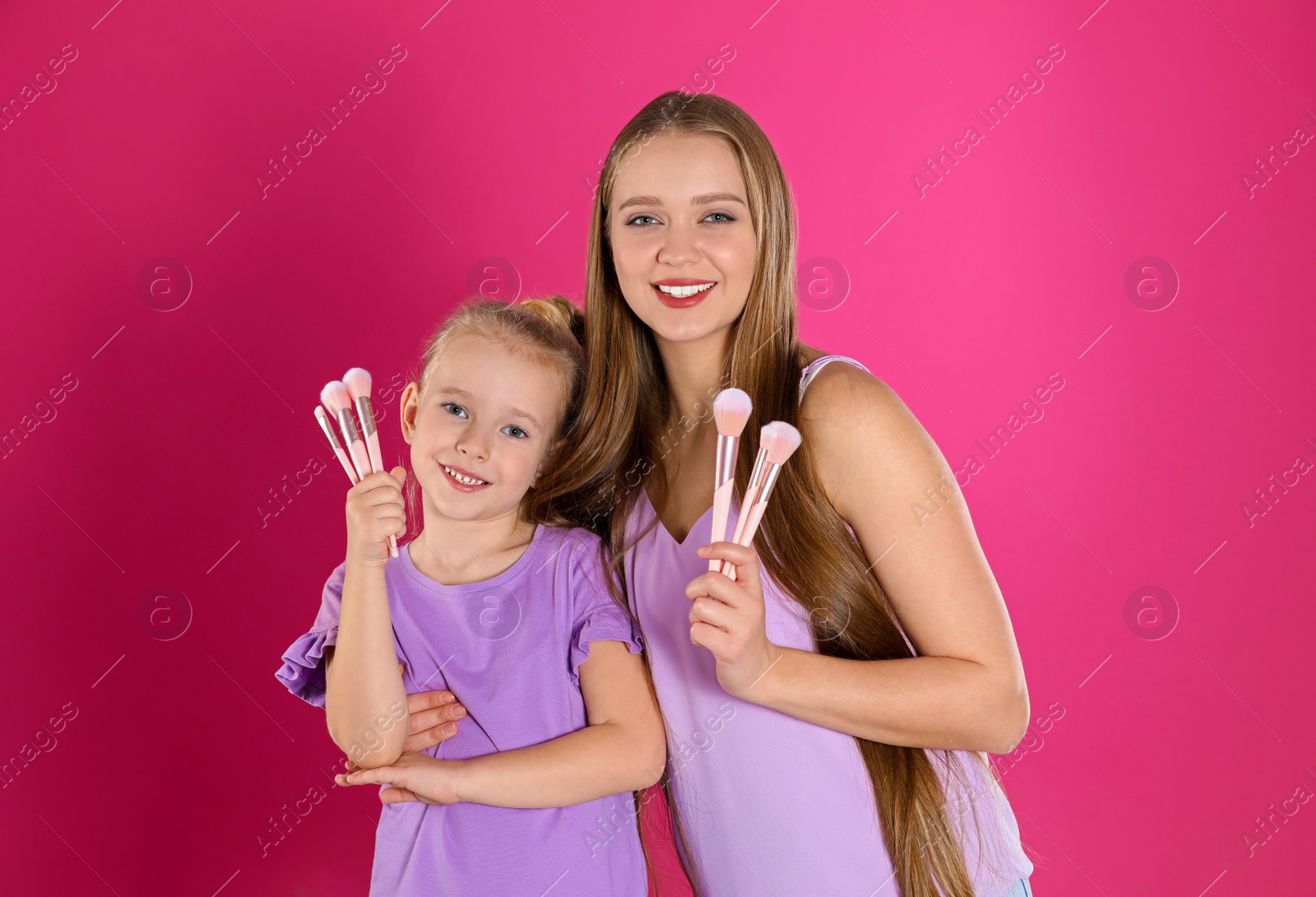 Photo of Happy mother and little daughter with brushes on pink background