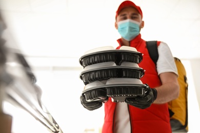 Courier in protective mask and gloves with order indoors, focus on hands. Restaurant delivery service during coronavirus quarantine