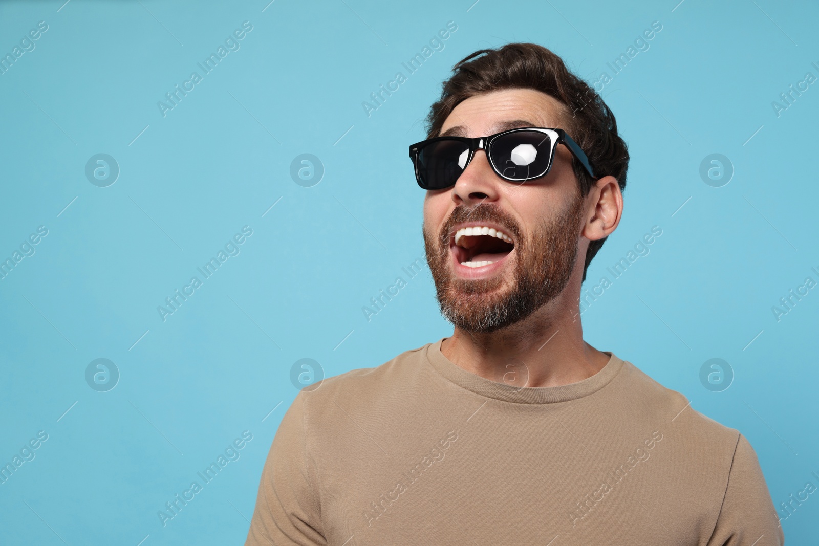 Photo of Portrait of excited bearded man with stylish sunglasses on light blue background. Space for text