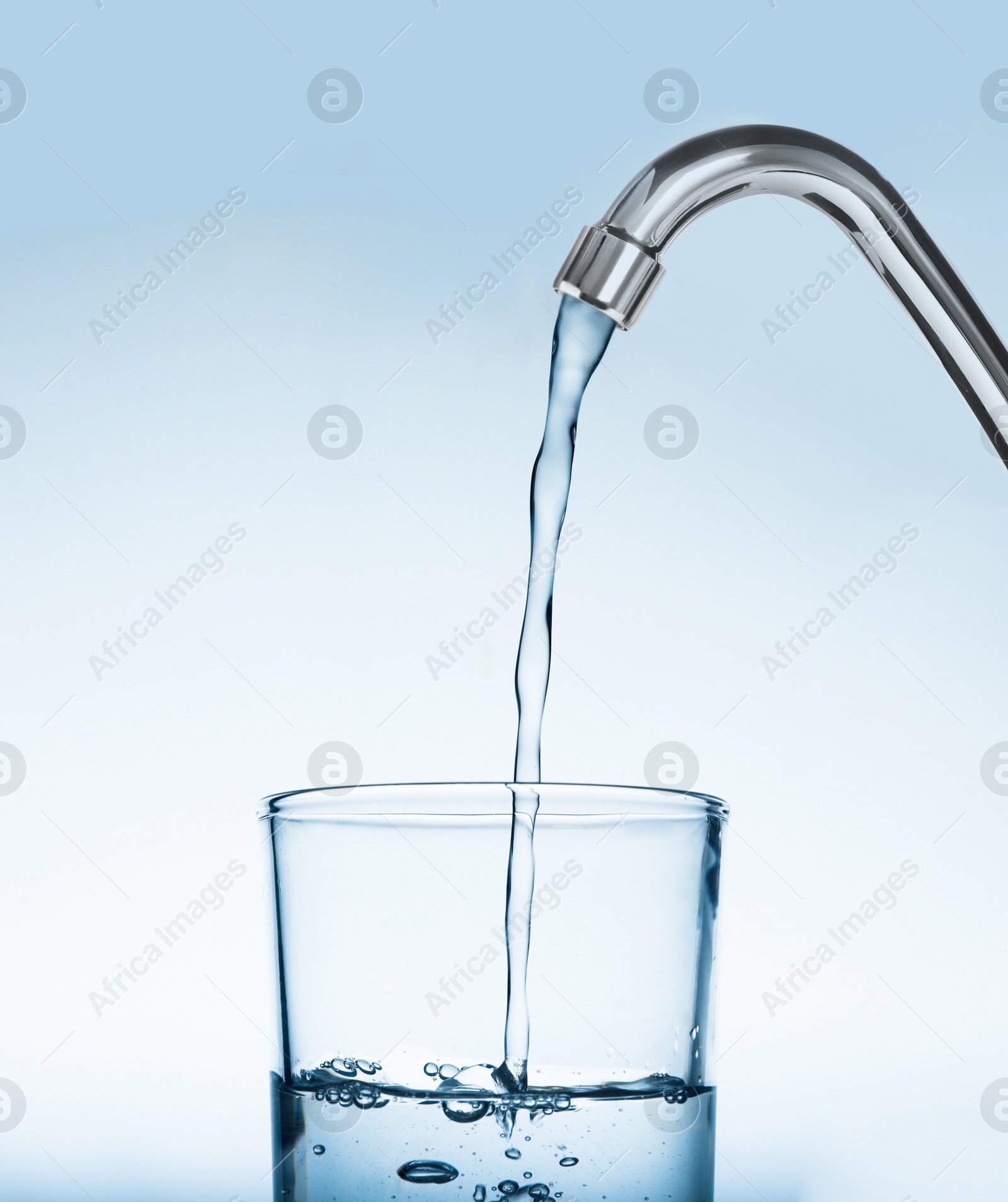 Image of Filling glass with water from tap on light blue background