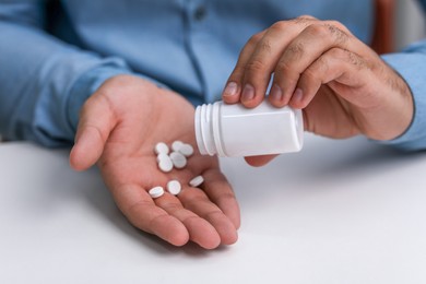 Photo of Man pouring antidepressants from bottle at white table, closeup