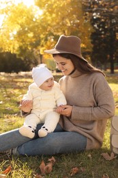 Happy mother with her baby daughter sitting on grass in autumn park