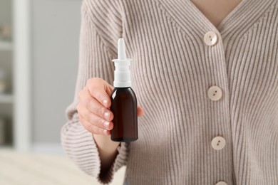 Woman holding nasal spray indoors, closeup view