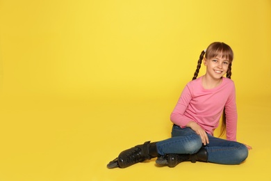 Girl with inline roller skates sitting on color background. Space for text