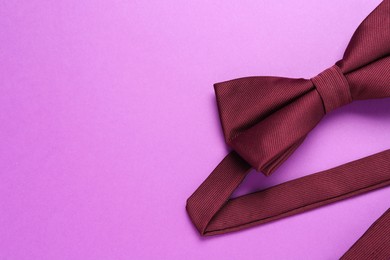 Photo of Stylish burgundy bow tie on violet background, top view. Space for text