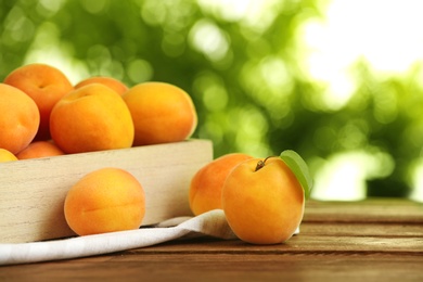 Crate and delicious ripe sweet apricots on wooden table against blurred background, space for text