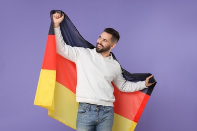 Photo of Young man holding flag of Germany on purple background