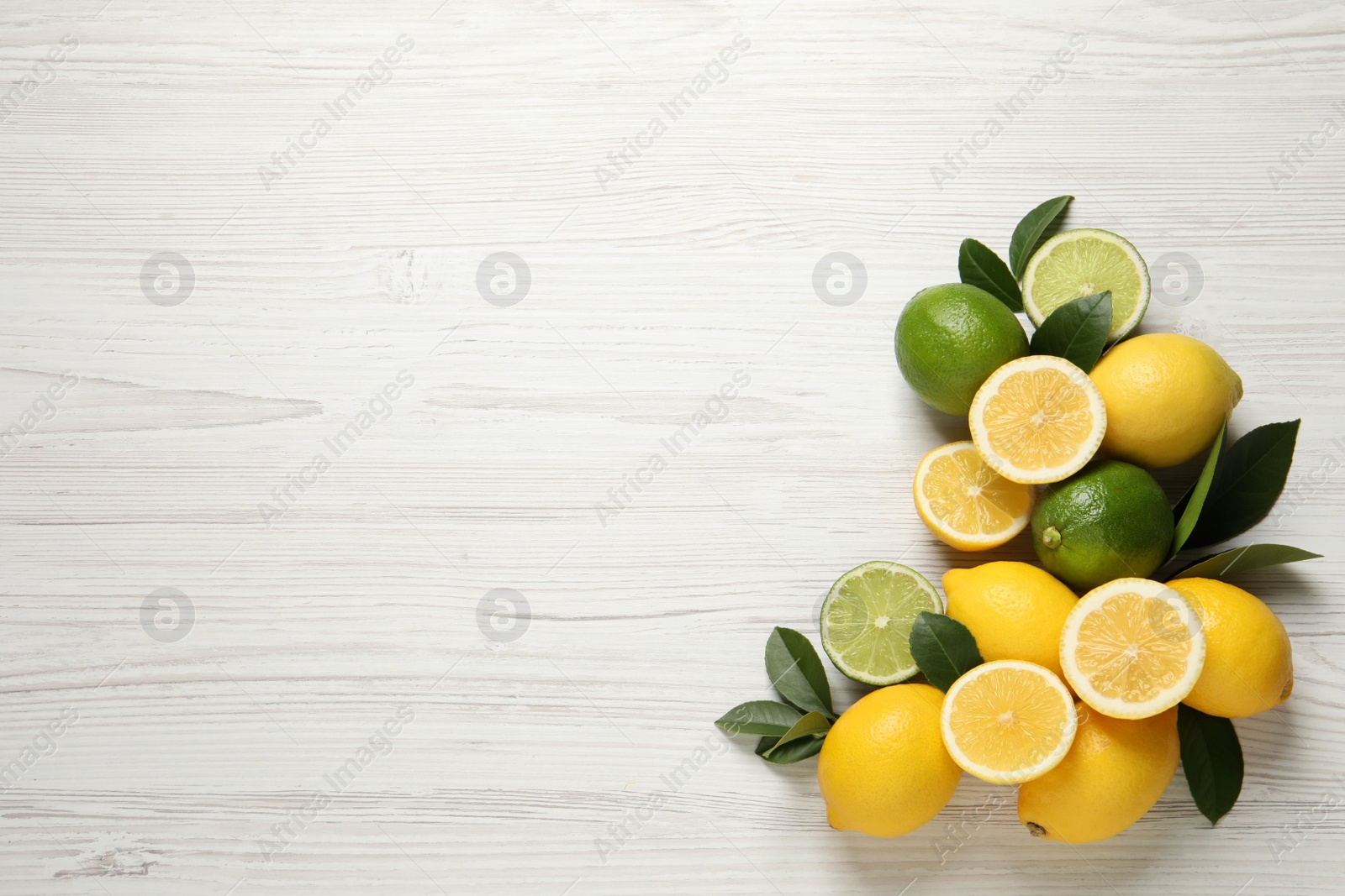 Photo of Fresh ripe lemons, limes and green leaves on white wooden background, flat lay. Space for text