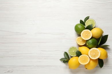 Fresh ripe lemons, limes and green leaves on white wooden background, flat lay. Space for text