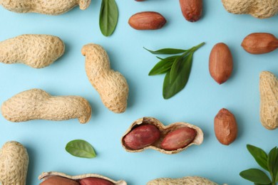 Photo of Fresh peanuts and leaves on light blue table, flat lay