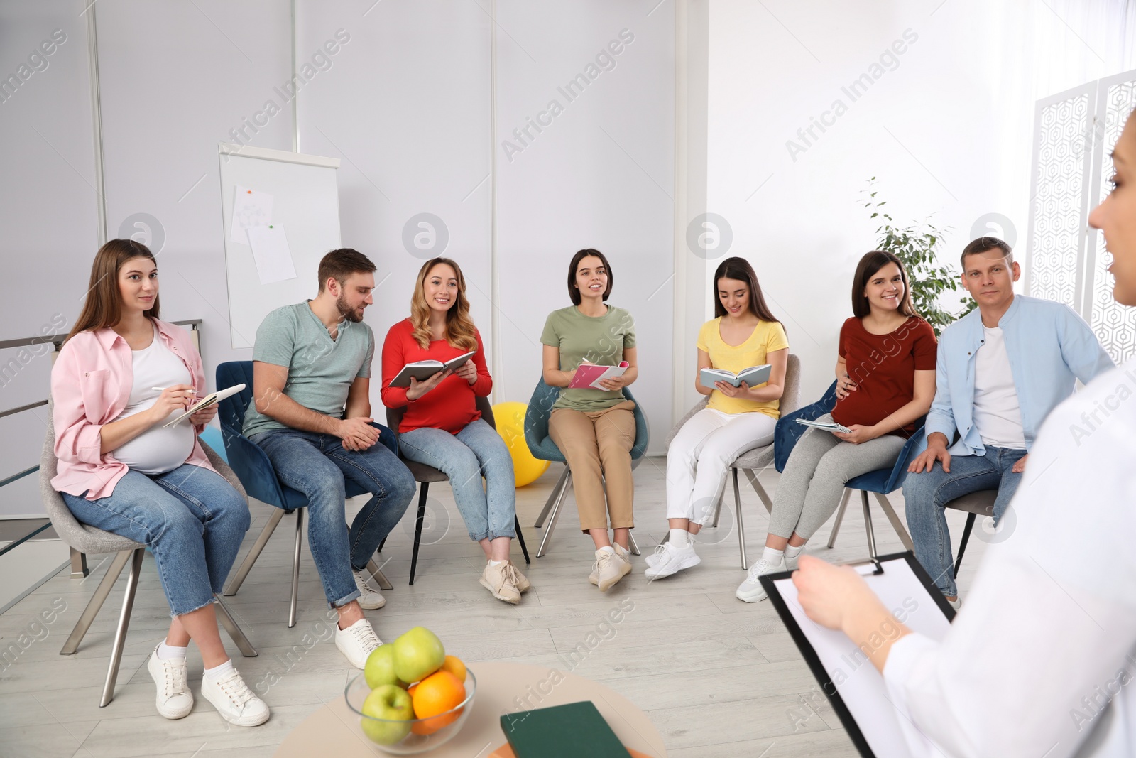 Photo of Group of pregnant women with men and doctor at courses for expectant parents indoors