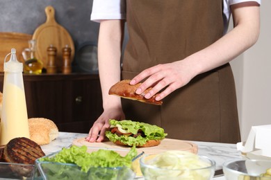 Woman making delicious vegetarian burger at white marble table, closeup