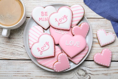 Photo of Decorated heart shaped cookies and coffee on white wooden table, flat lay. Valentine's day treat