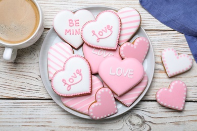 Decorated heart shaped cookies and coffee on white wooden table, flat lay. Valentine's day treat